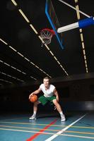 stoere gezonde jonge man spelen basketbal in de sportschool binnen. foto