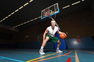stoere gezonde jonge man spelen basketbal in de sportschool binnen. foto
