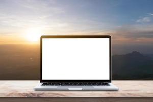 moderne laptopcomputer met leeg scherm op houten tafel over berg bij zonsopgang hemelachtergrond. foto