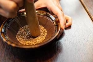 Japanse sesam maalkom en houten stok. houten kom met witte sesam voor het malen op houten tafel. stokje voor Japanse varkenskotelet foto