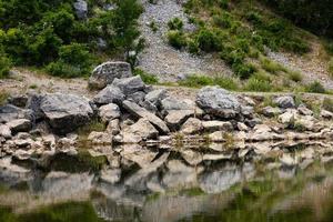 uitzicht op de kustlijn van een bergmeer op de voorgrond met grote stenen en reflectie in het water. landschap. foto