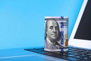 laptop met een rol papier honderd-dollarbiljetten op een blauwe achtergrond. ruimte kopiëren. foto