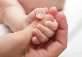 close-up van een baby die de duim van een volwassene houdt foto