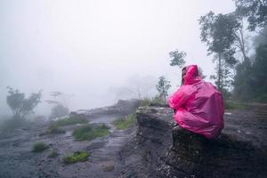 toerist met roze regenjas zittend uitzicht op het landschap natuurlijke mooie aanraking mist in phu hin rong kla nationaal park. reizen natuur, reizen ontspannen, reizen thailand, regenseizoen. foto