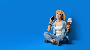reizigersmeisje in een blauwe jurk lacht blij met een vrolijk gezicht en houdt een paspoort vast met mobiele telefoons in de hand, op een blauwe kleurachtergrond. concept reizen foto