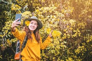 een meisje met een rugzak gebruikt de telefoon om een foto te maken van de gele bua tong-bloem. Mexicaanse zonnebloem