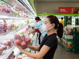 aziatische vrouw met een beschermend gezichtsmasker en rubberen handschoenen die voedsel winkelen foto
