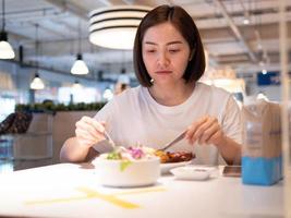 aziatische vrouw die gescheiden zit in restaurant eten eten met tafelschild plastic scheidingswand om infectie te beschermen tegen coronavirus covid-19 foto