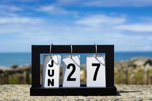 27 juni kalender datum tekst op houten frame met onscherpe achtergrond van de oceaan. foto