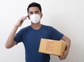 gelukkige bezorgservicemedewerker met medisch gezichtsmasker draagt kartonnen doos in de hand foto