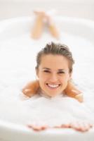glimlachende jonge vrouw die in badkuip legt