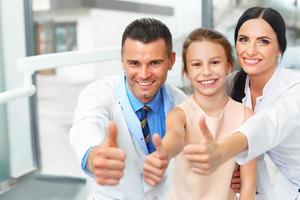tandarts arts, assistent en klein meisje glimlachen allemaal op camera foto