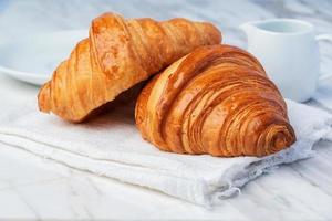 verse croissants brood en een kopje koffie op stof. foto