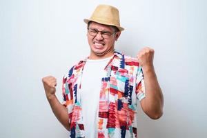 jonge knappe man met een casual strandshirt die erg blij en opgewonden staat en een winnaargebaar maakt met opgeheven armen foto