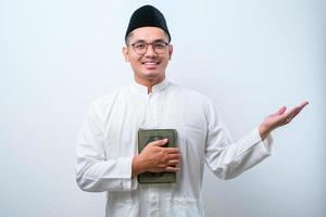 aziatische moslimman die lacht met het al-koranboek in handen en iets aan zijn zijde laat zien foto