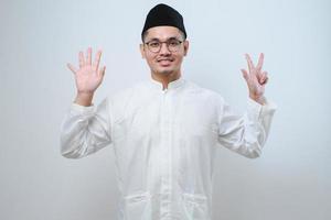Aziatische moslimman die vrijetijdskleding draagt en omhoog wijst met vingers nummer acht terwijl hij zelfverzekerd en gelukkig glimlacht foto
