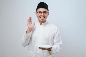 Aziatische moslimman die opgewonden uitdrukking toont terwijl hij een leeg bord vasthoudt foto