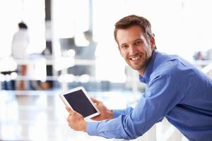 portret van man in kantoor met behulp van tablet glimlachen naar camera