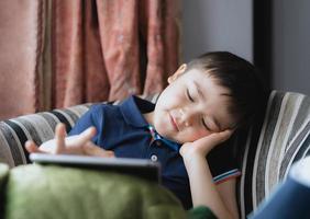 filmisch portret jonge jongen speelt een spel op tablet zittend op de bank met licht dat uit het raam schijnt, kind speelt online spelletjes op internet thuis, kind praat videogesprek met vrienden thuis foto