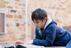 schoolkind doet huiswerk leesboek, portret jonge jongen zit alleen buiten een verhaal te lezen, onderwijsconcept foto