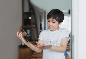 filmisch portret gelukkige jonge jongen die karton gebruikt voor hoofdtelefoonspeelgoed, actief kind met grote glimlach tijdens het spelen van een kaartdoos, positief kind dat thuis ontspant in het weekend, diy recyclingspeelgoedidee voor kinderen foto