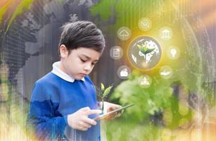 schoolkind met behulp van tabletonderzoek op internet over wereldbevolking, ecologie en milieu, jongen die online leert, aardrijkskunde met dubbele belichtingsgroei futuristische jonge groene boom op wereldbolkaart foto