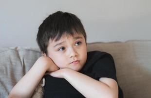 portret jonge jongen die diep in gedachten kijkt, schooljongen die uitkijkt met een denkend gezicht. close-up kind met nieuwsgierig gezicht alleen zittend op de bank. foto