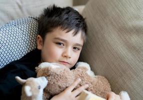 gelukkige jongen liggend op de bank kijkend naar de camera met lachend gezicht, positief kind rustend in de woonkamer met fel licht schijnt uit raam op zonnige dag lente of summer.kid ontspannen thuis in het weekend foto