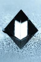 close-up beeld van een natte glazen piramide. glanzende piramide met druppels water. foto