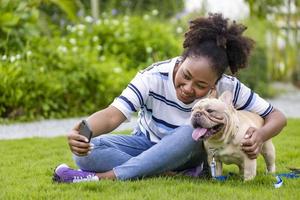 Afro-Amerikaanse vrouw neemt selfie met haar Franse bulldog-puppy terwijl ze in het grasveld ligt na 's ochtends te hebben geoefend in het park foto