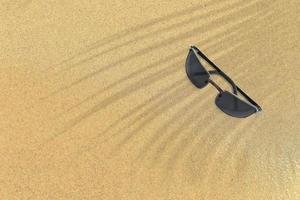 top-up weergave van zwarte zonnebril op zandstrand. vakantie concept achtergrond. foto