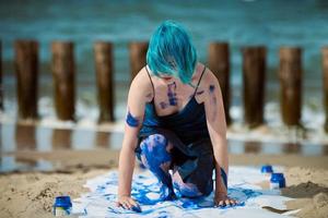 artistieke blauwharige vrouwelijke performancekunstenaar besmeurd met gouacheverf op groot doek op strand foto