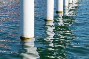 roestige pijlerposten in zout zeewater. witte kolommen diagonaal. pijlers monteren voor brug. zonnig weer. foto