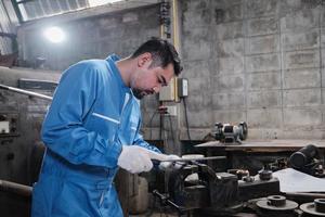 een professionele Aziatische mannelijke industrie-ingenieur werkt in een veiligheidsuniform met precisiegereedschappen voor metaalbewerking, mechanische draaimachines en een werkplaats voor reserveonderdelen in de staalfabriek. foto