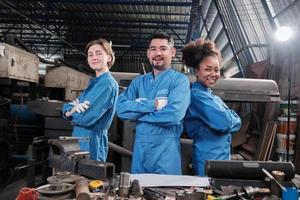 multiraciale industriearbeiders in veiligheidsuniformen werken samen met eenheid, armen gekruist en drukken gelukkig werk uit samen met een glimlach en vrolijk in mechanische fabriek, professionele ingenieursbezetting. foto