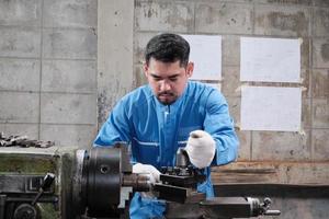 een professionele Aziatische mannelijke industrie-ingenieur werkt in een veiligheidsuniform met precisiegereedschappen voor metaalbewerking, mechanische draaimachines en een werkplaats voor reserveonderdelen in de staalfabriek. foto