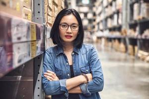 Aziatische mooie jonge vrouw werknemer van meubelwinkel met gekruiste armen in een groot magazijn.