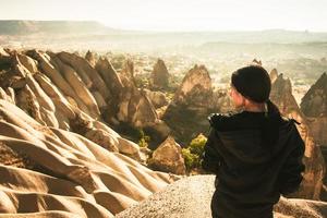 doordachte vrouwelijke persoon kijkt uit over dramatische vallei op wazige ochtendzonsopgang met sprookjesachtige schoorstenen achtergrond. solo-exploratie in turkije. filmische reisbestemming-cappadocië foto