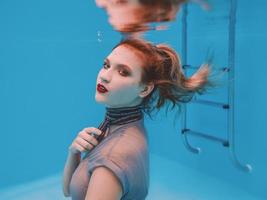 surrealistisch kunstportret van een jonge vrouw in een grijze jurk en een sjaal met kralen onder water in het zwembad foto