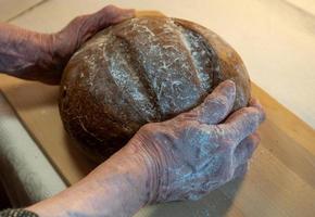 zwart vers brood in de handen van een oudere vrouw op een keukenbord. foto