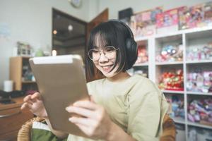 jonge volwassen aziatische vrouw draagt een koptelefoon, luistert naar muziek en ontspant met behulp van een digitale tablet om op het net te surfen foto