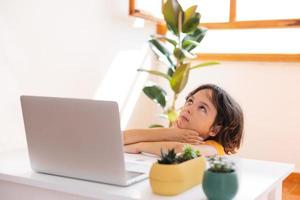 portret van een verveelde jongen, kindjongen gebruikt een laptop en studeert online foto