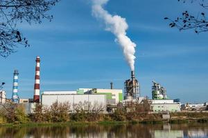 pijpen van houtbewerking onderneming plant zagerij in de buurt van rivier. luchtvervuiling concept. industrieel landschap milieuvervuiling afval van thermische elektriciteitscentrale foto