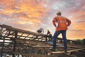 ingenieur inspecteert, installateurs, repareert daken boven de wolken, blauwe lucht, technici installeren dakbedekking aan de bovenkant van het huis, renoveren, renoveren, bouw een landhuis foto