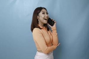 een portret van een vrolijke jonge Aziatische vrouw die een telefoongesprek voert, geïsoleerd op een blauwe achtergrond foto