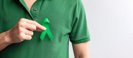 hand met groen lint voor lever, galblaas, galwegen, baarmoederhalskanker, nierkanker en lymfoom bewustzijnsmaand. gezondheidszorg en wereld kanker dag concept foto