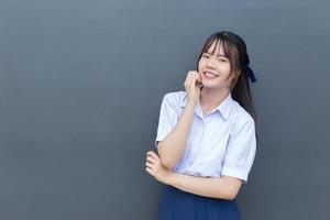 mooie Aziatische middelbare school student meisje in het schooluniform met een zelfverzekerde glimlach terwijl ze gelukkig naar de camera kijkt met grijs op de achtergrond. foto