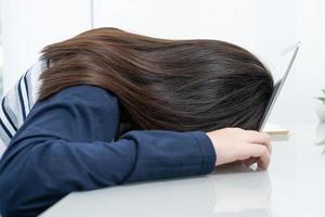 jonge vrouw lang haar valt in slaap op bureau met laptop foto