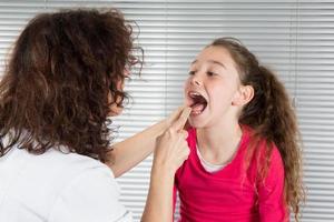 vrouw arts onderzoekt de keel van een jong meisje