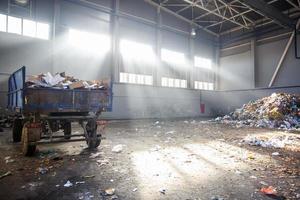 afvalsorteer- en recyclingwerkplaats met aanhanger bij de afvalverwerkingsfabriek met zonnestralen. gescheiden afvalinzameling. recycling en opslag van afval voor verdere verwijdering. foto